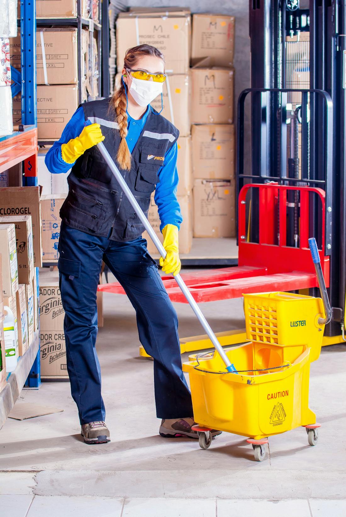 Professional cleaner with a mop and cleaning trolley in a commercial corridor